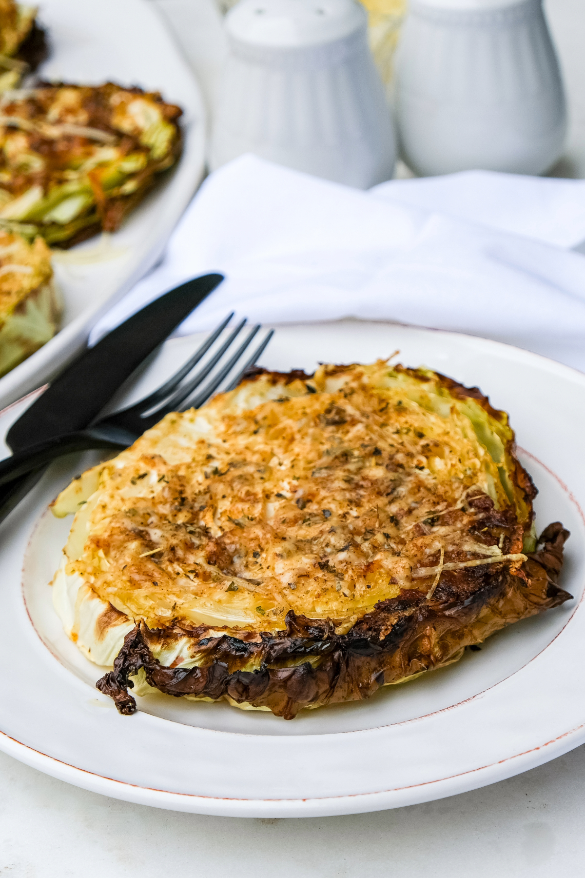 A slice of cooked cabbage topped with parmesan cheese on a white dinner plate.