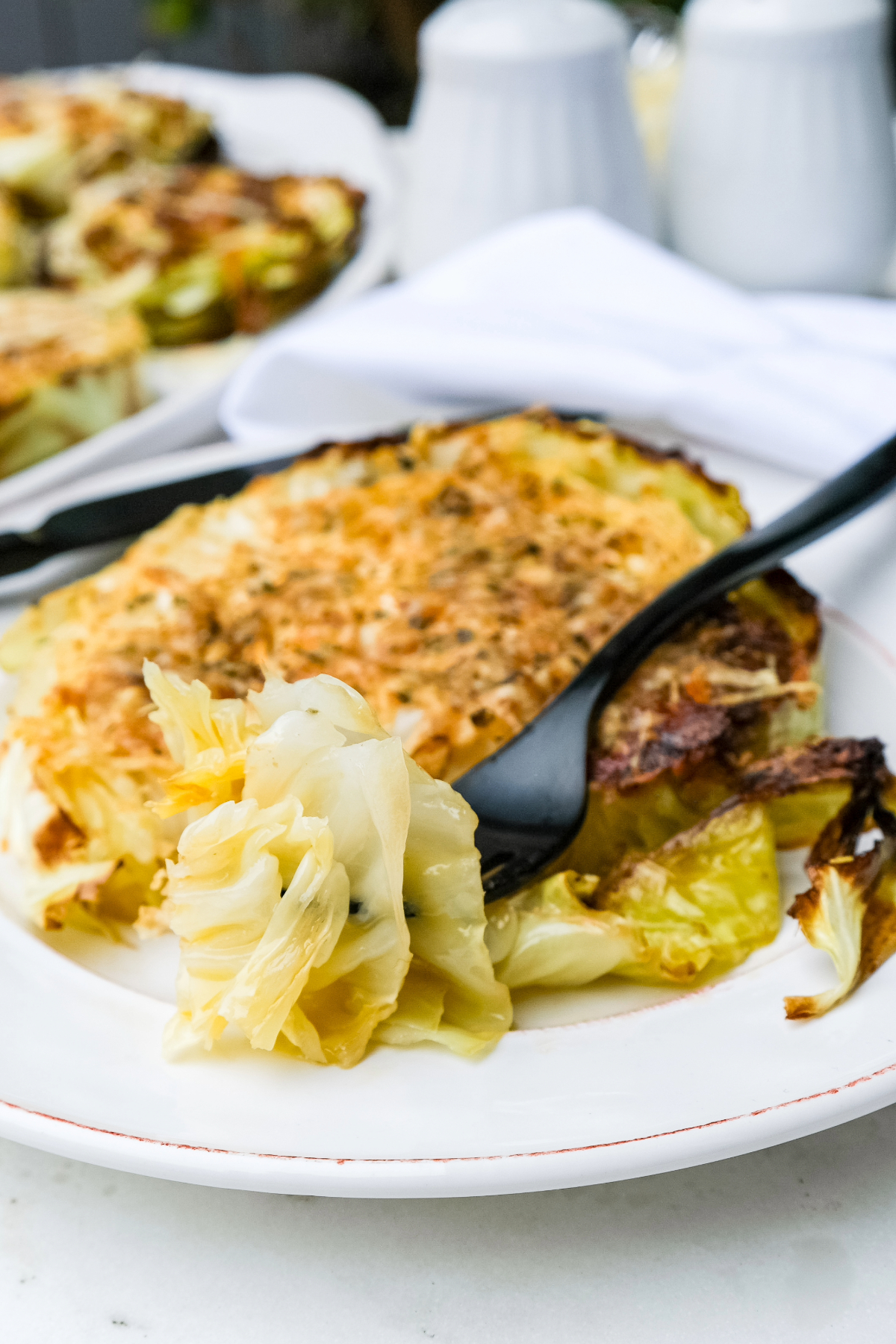 A slice of cooked cabbage on a dinner plate being picked up with a fork.