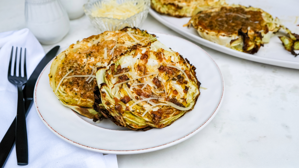 A dinner plate with a fork and knife next to roasted cabbage steaks.