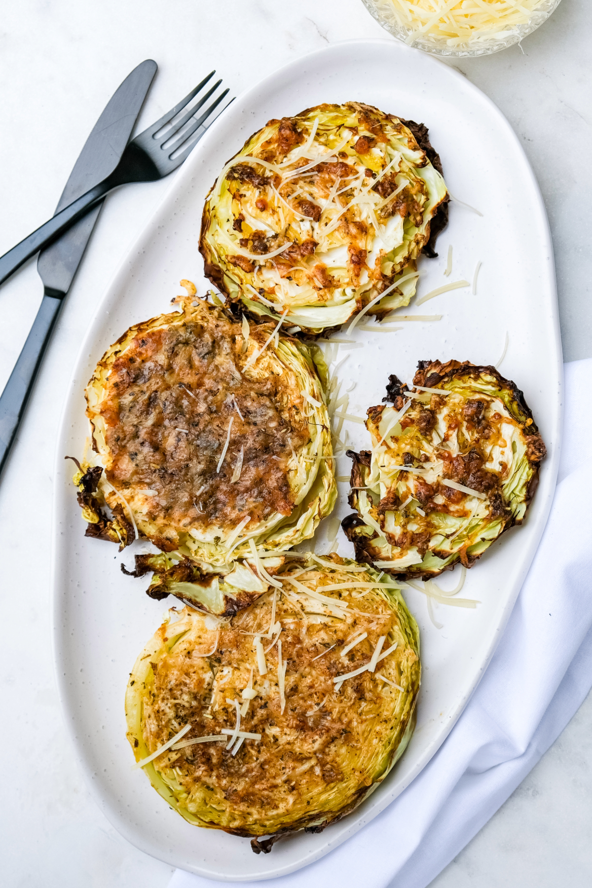 Overhead view of sliced cabbage on a white serving dish topped with parmesan cheese.