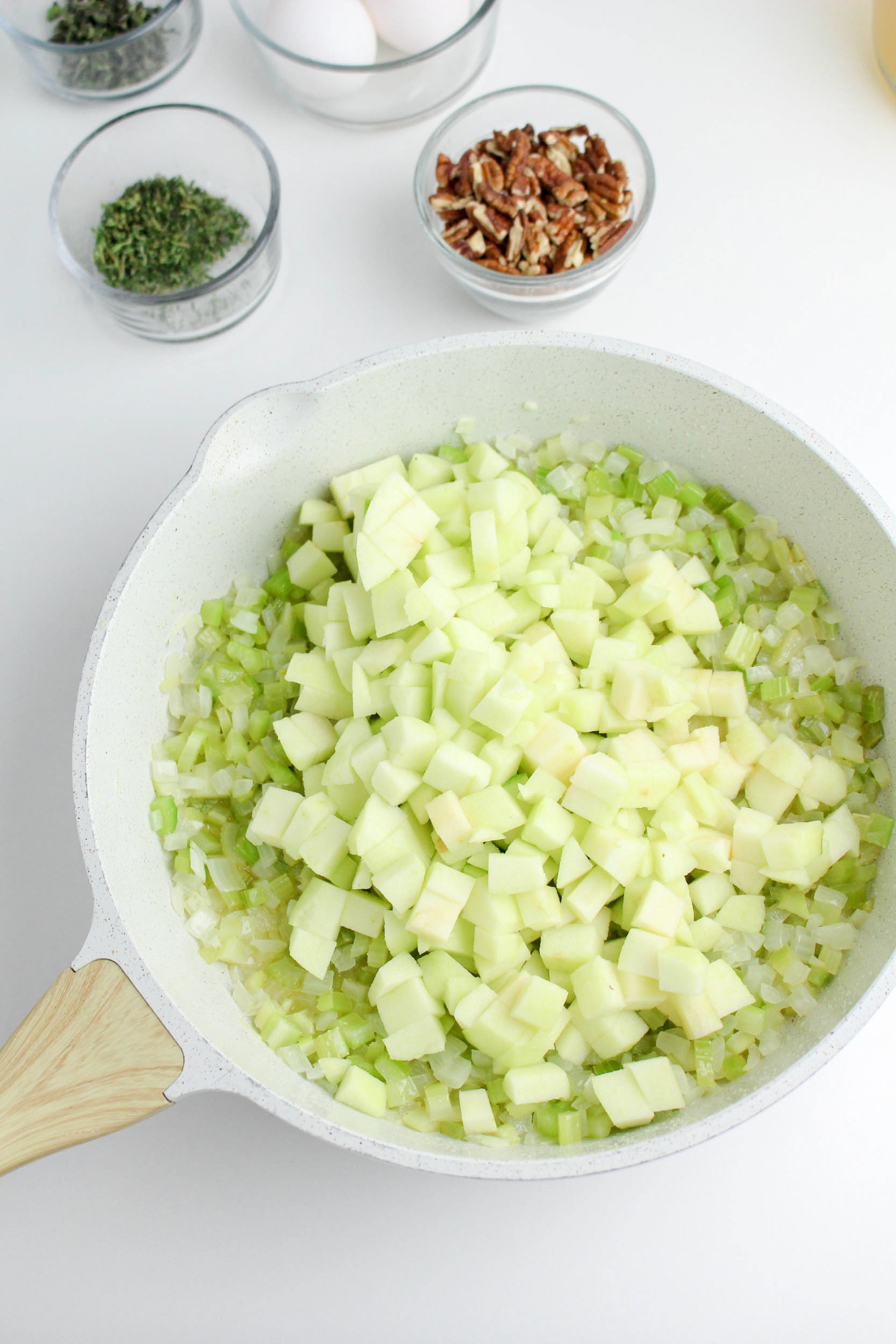 A white skillet with sauteed onions, celery and apple chunks.