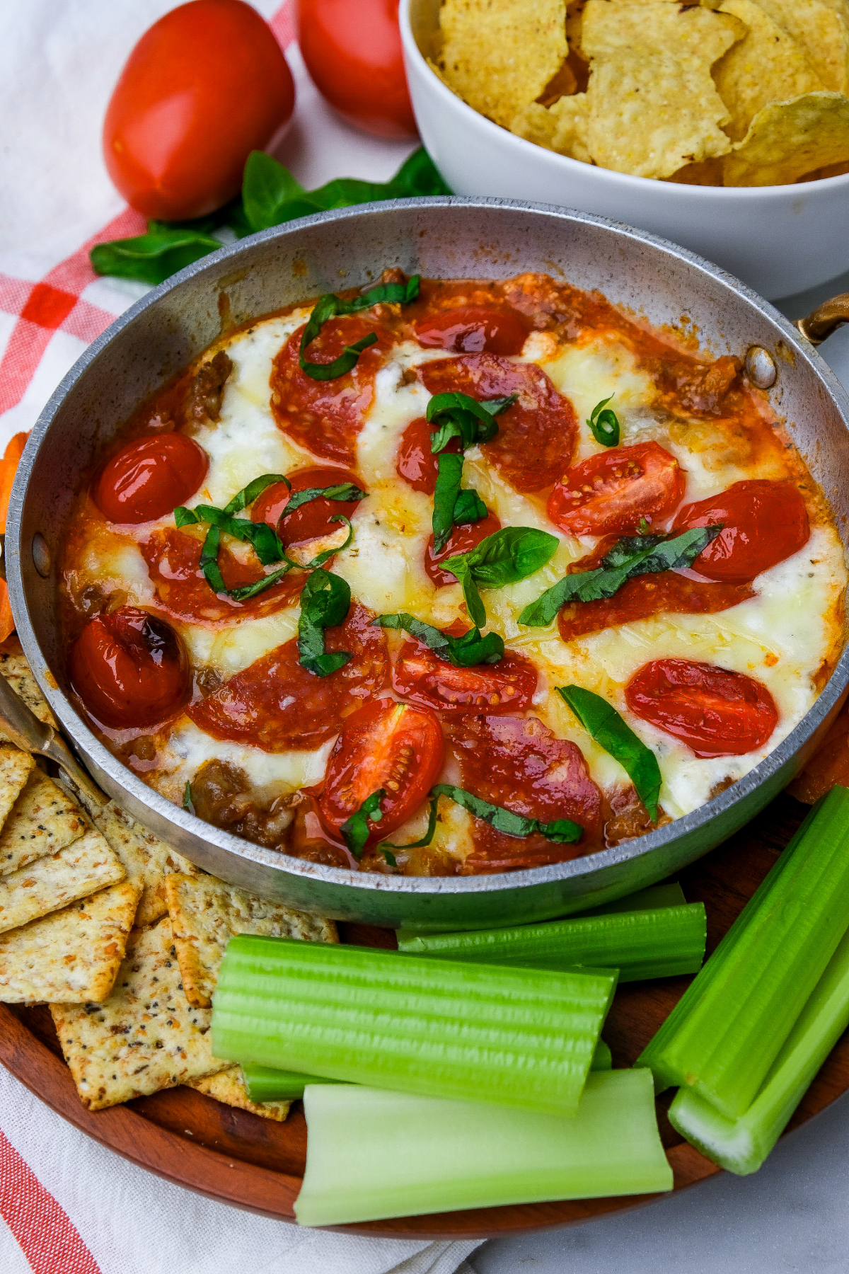A round stainless bowl with melted cheese topped with pepperoni, tomatoes, and basil.