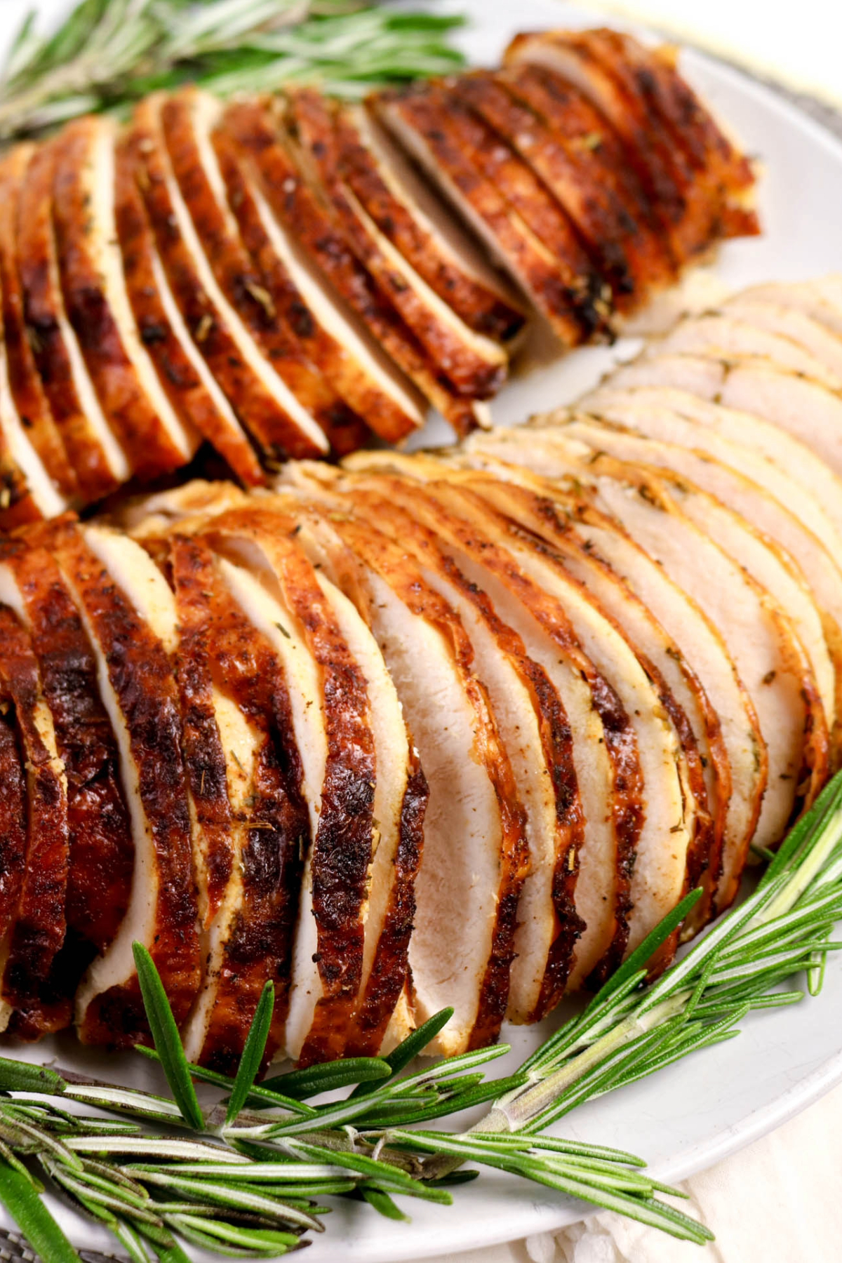 Close view of sliced turkey on a white plate with a sprig of rosemary.