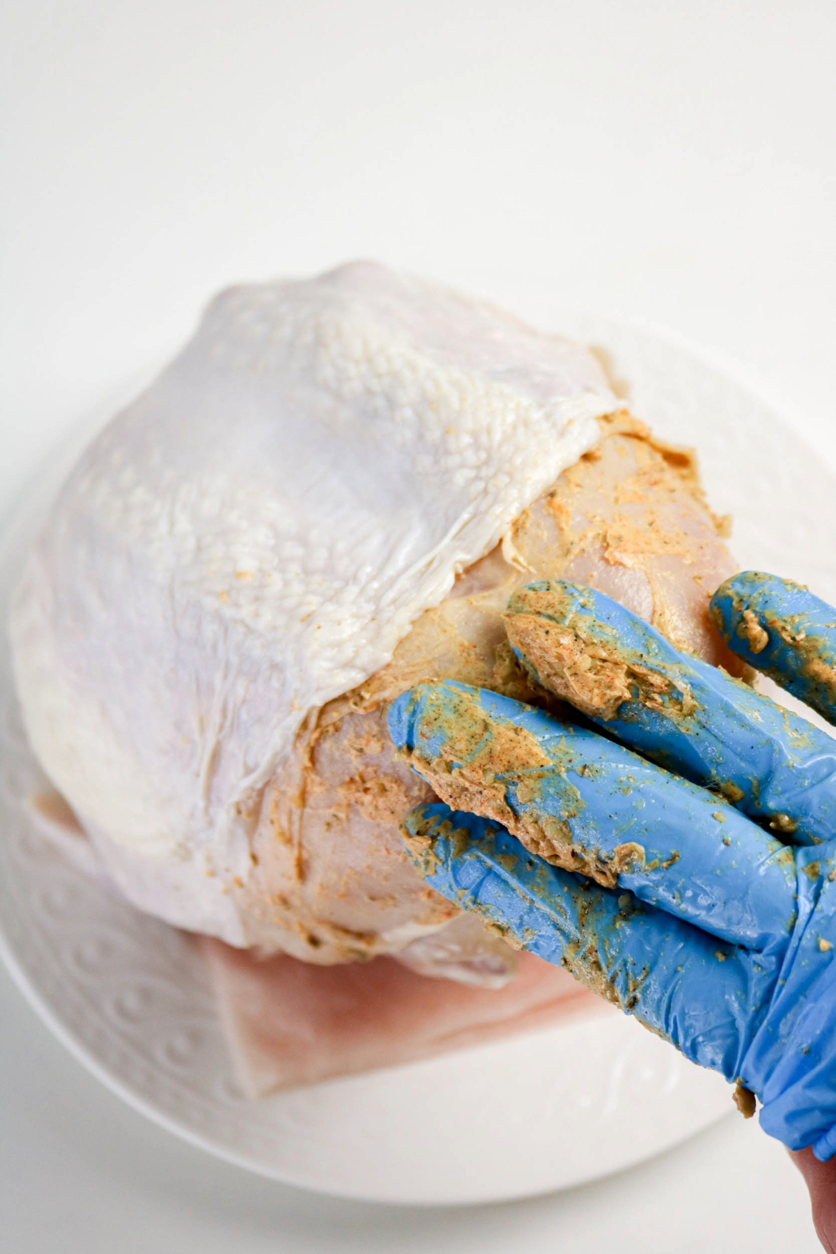 Preparing turkey breast before cooking by placing butter mixture between the skin and meat with a blue glove on.