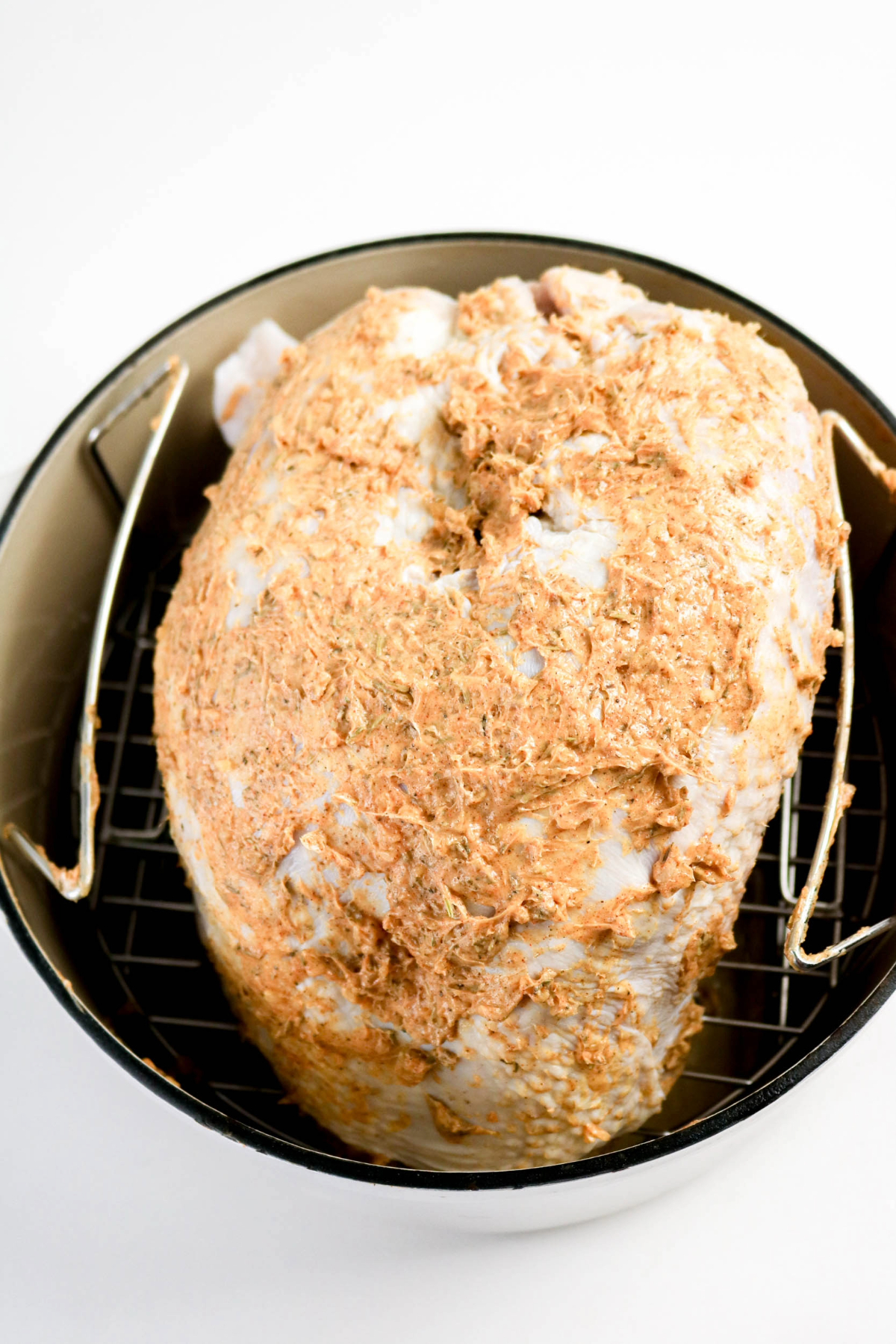Uncooked turkey breast in a baking pan with topped butter and seasonings.
