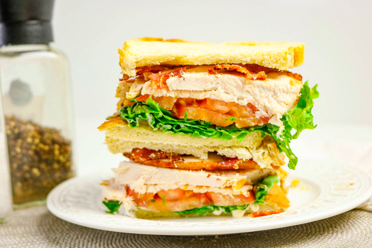 A stacked turkey sandwich with bacon, tomato, and lettuce on a white plate.