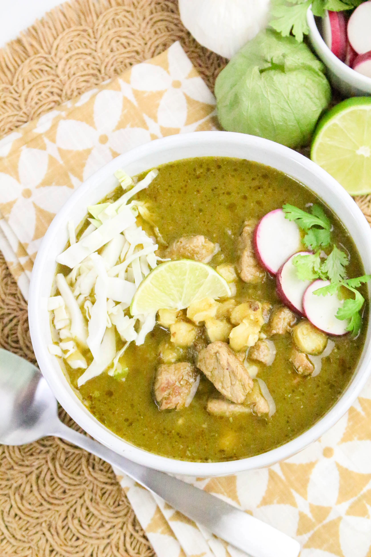 A white bowl with pork verde pozole topped with cabbage and radish slices.