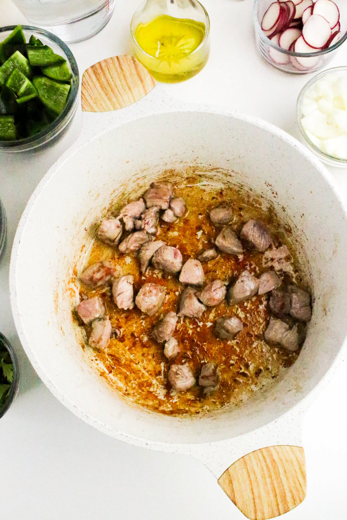 Browning diced pork in a white stockpot.