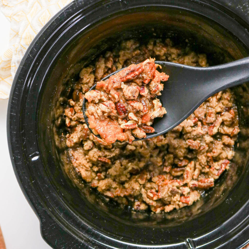 A spoon full of sweet potato casserole scooping out of a black slow cooker.
