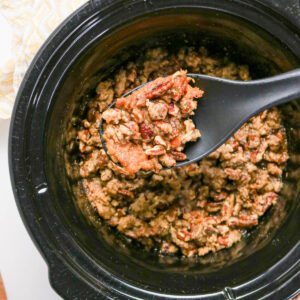 A spoon full of sweet potato casserole scooping out of a black slow cooker.