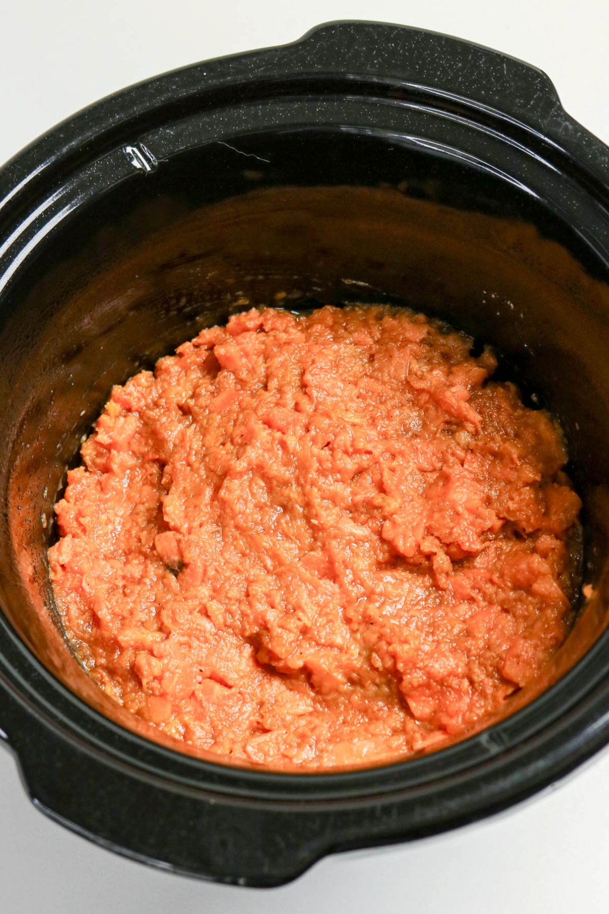 Mashed sweet potatoes layered on the bottom of a black slow cooker insert.