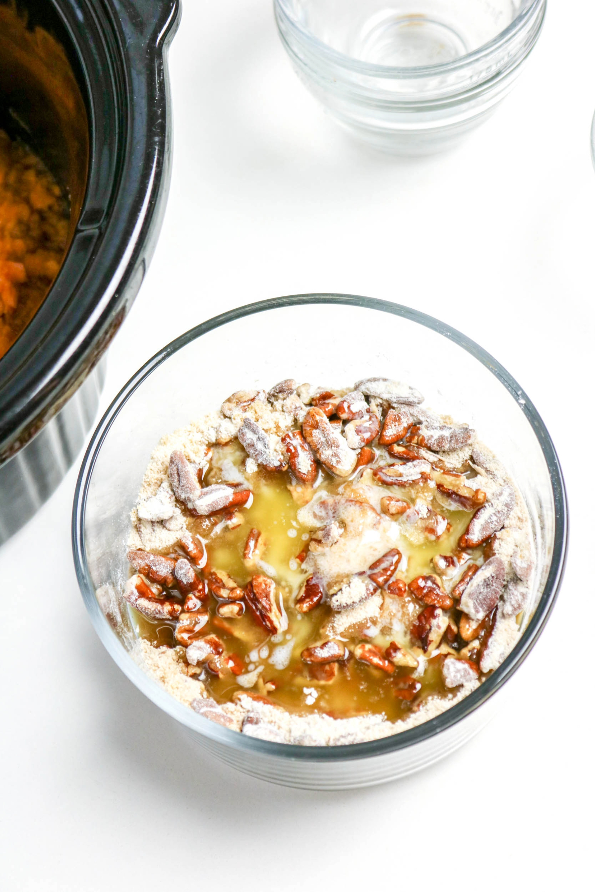 Small clear mixing bowl of pecans, butter, sweetener and flour for topping of sweet potato casserole dish.