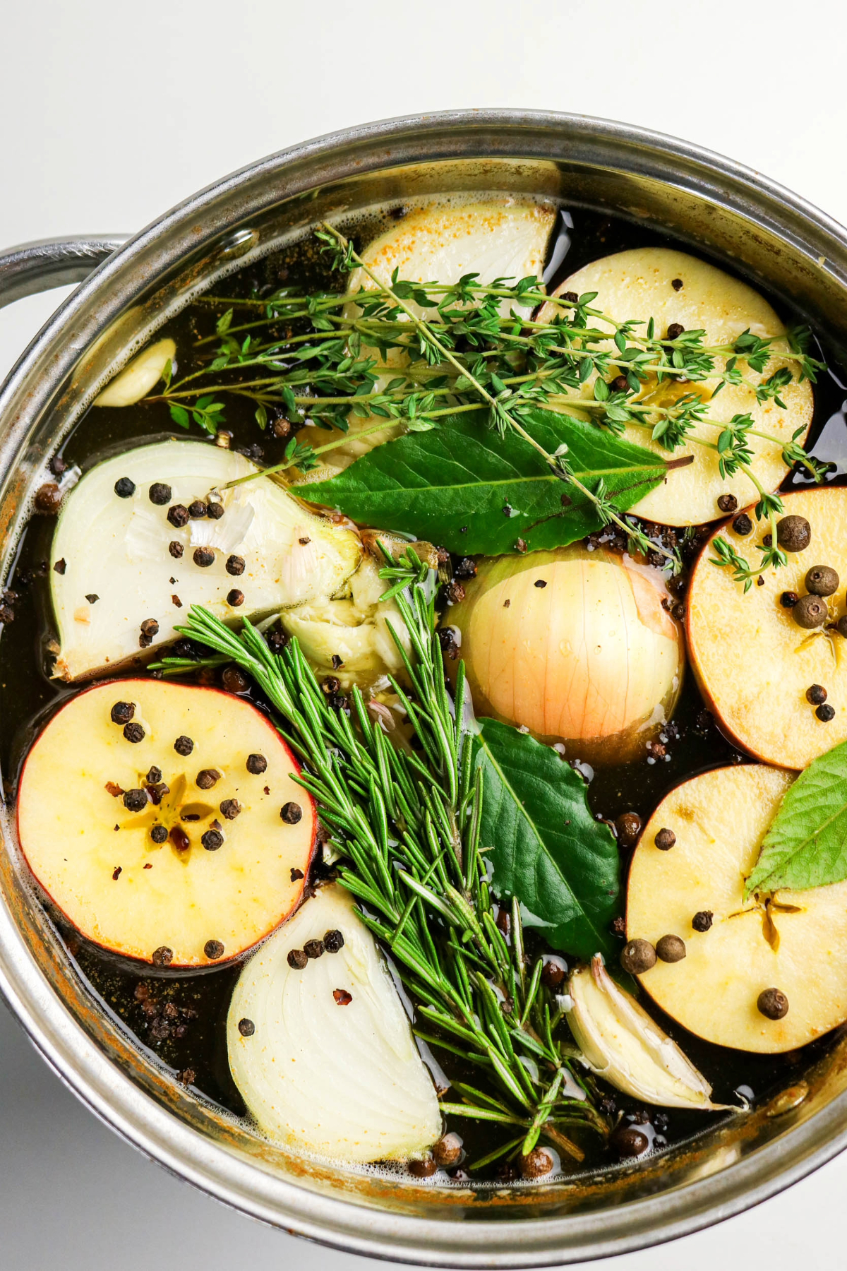 Spices, onion, and sliced apples with herbs in a brine mixture.