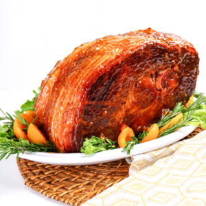 A whole ham on a white platter with sliced apricots around the ham.