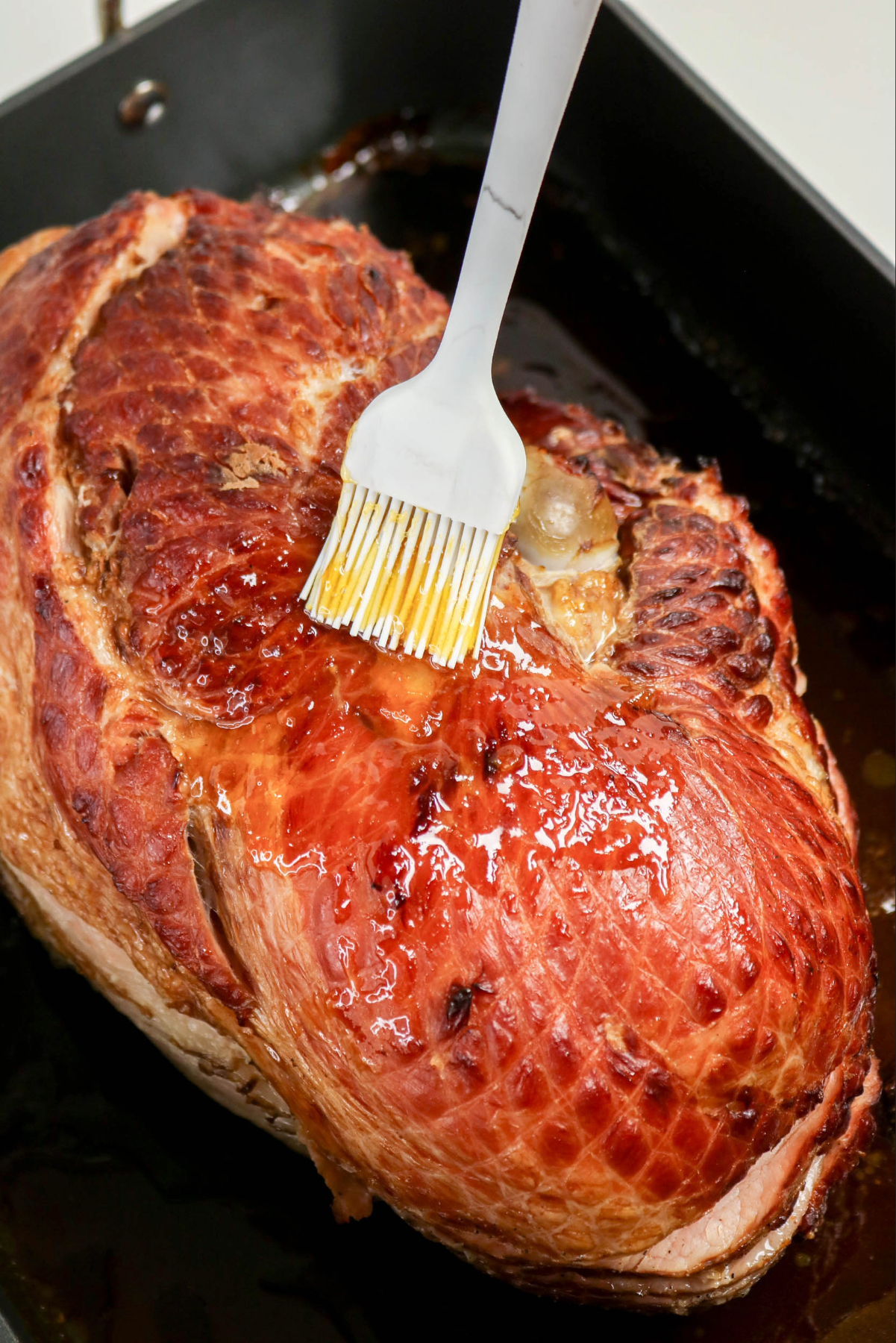 Brushing apricot glaze on a ham in a roasting pan.
