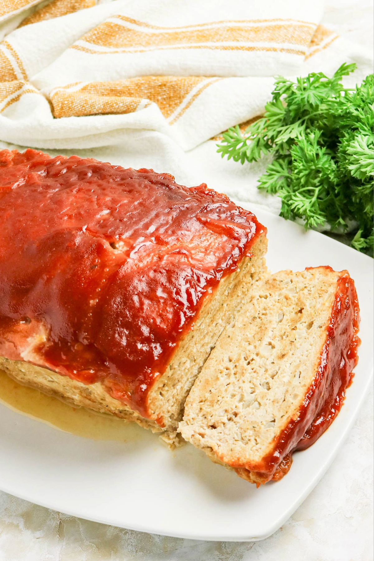 A loaf of chicken meatloaf topped with a ketchup and dijon mustard glaze on a white serving platter.
