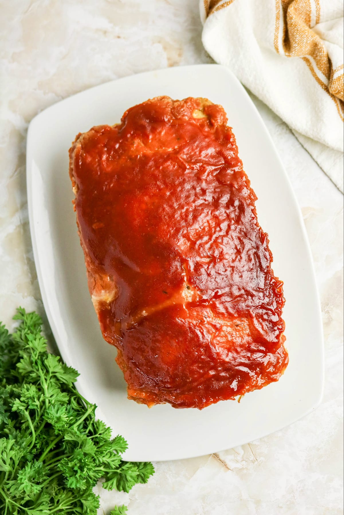 Overhead view of meatloaf on a white serving plate.