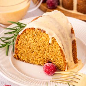 A slice of eggnog bundt cake on a white plate with a cup of eggnog in the background.