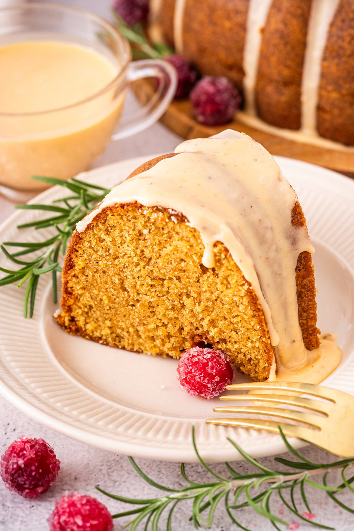 A slice of eggnog cake topped with a glaze and sugar cranberries. 