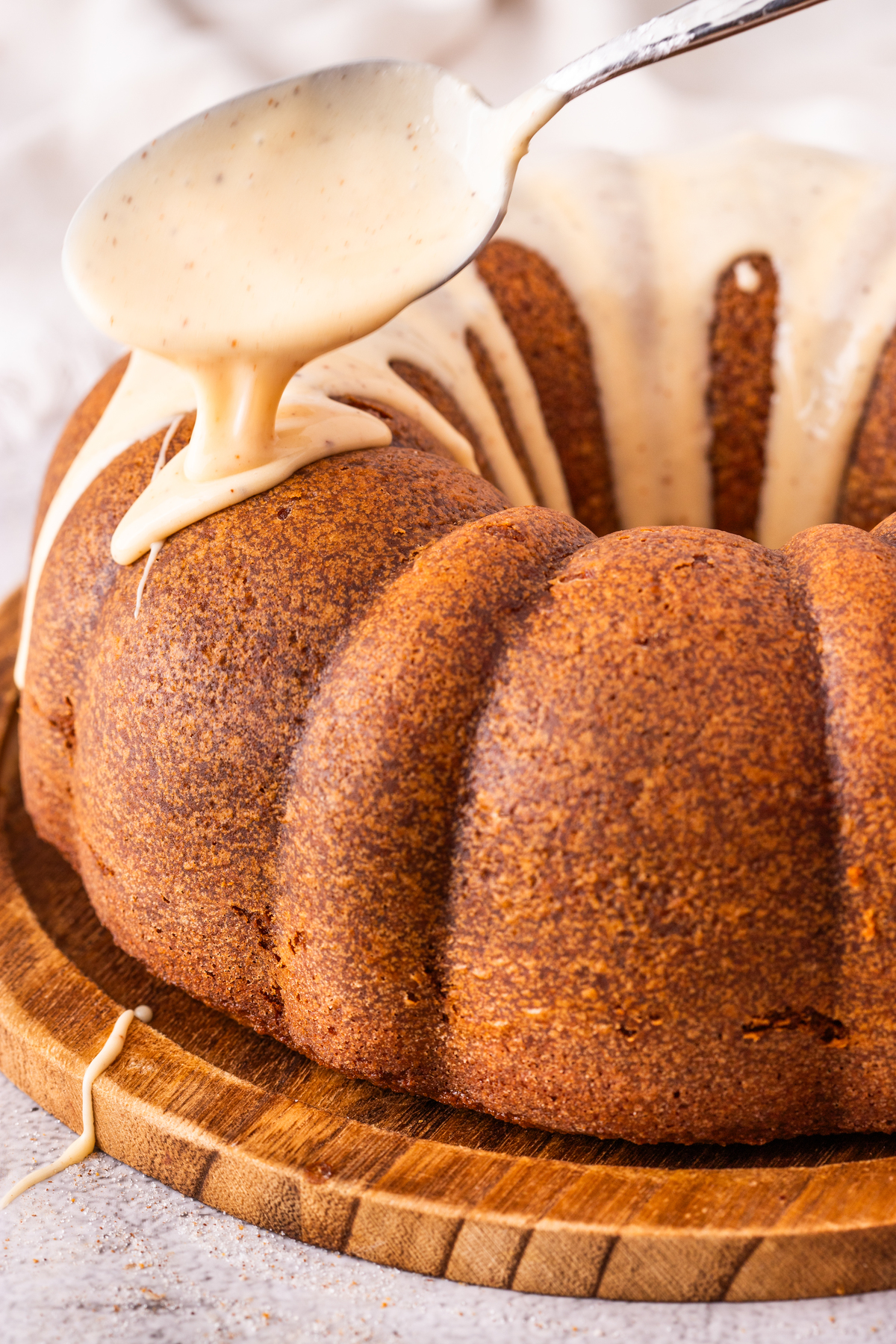 A spoonful of eggnog glaze dripping on prepared bundt cake. 