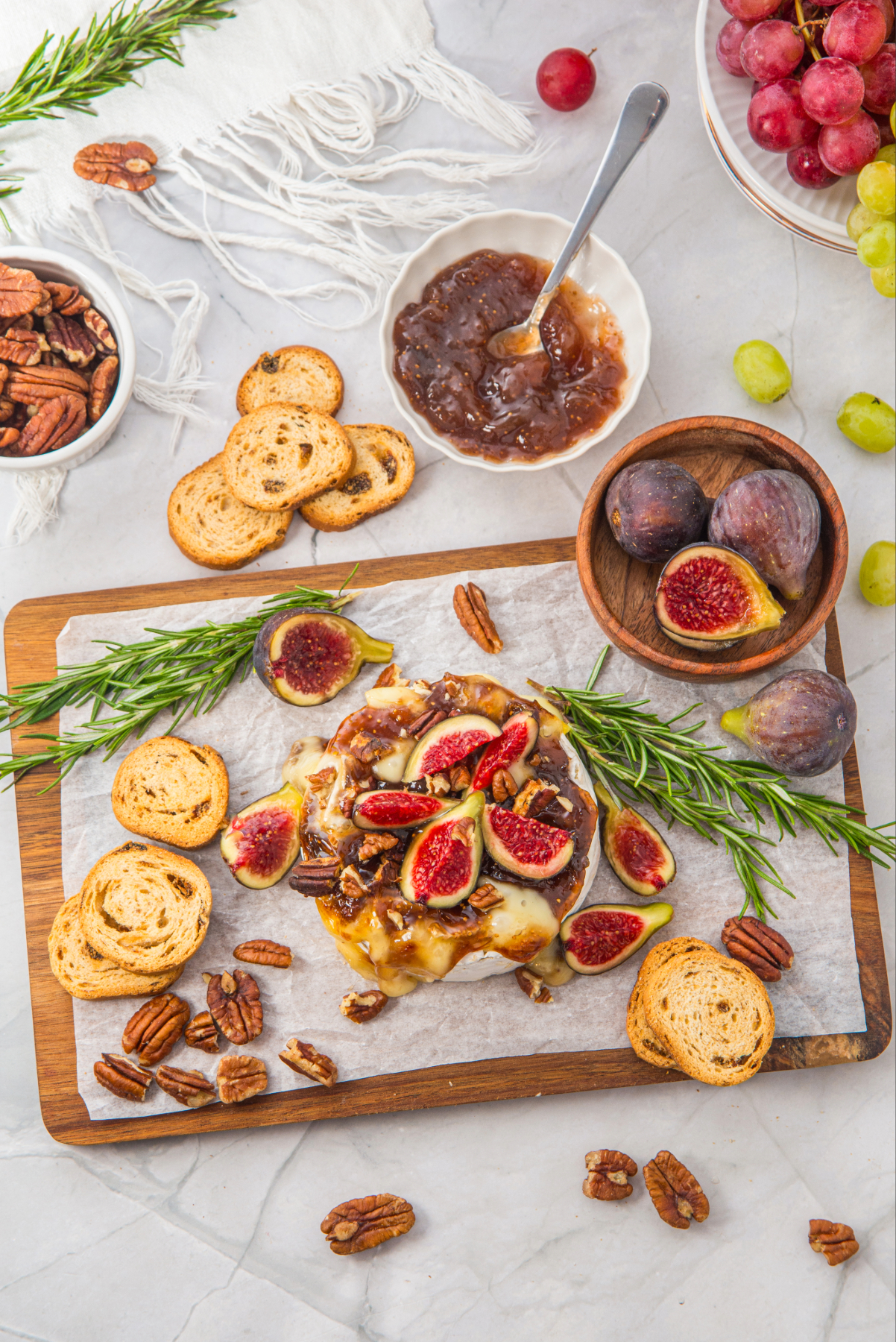 Overhead view of brie topped with figs and pecans on a cutting board.