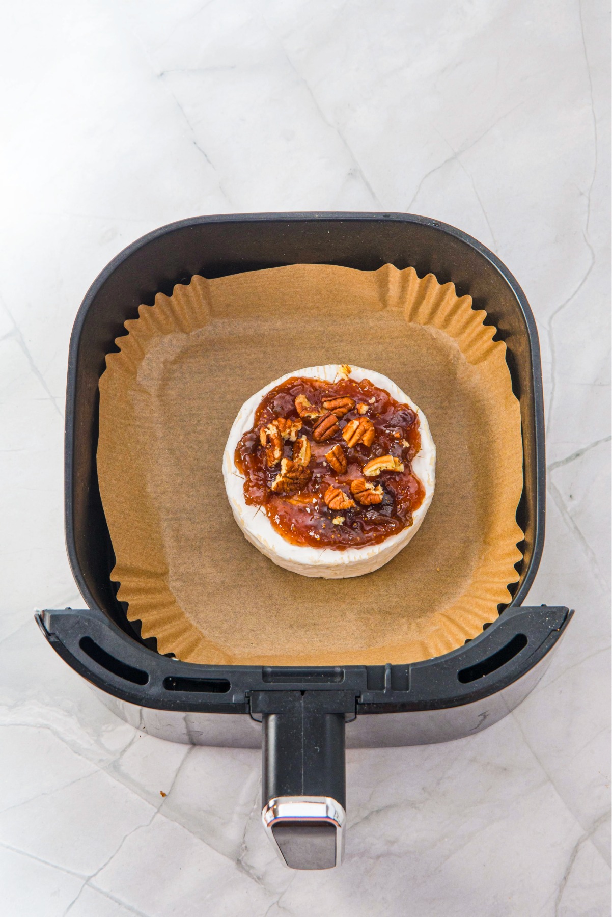 A wheel of brie in an air fryer topped with fig jam and pecans.