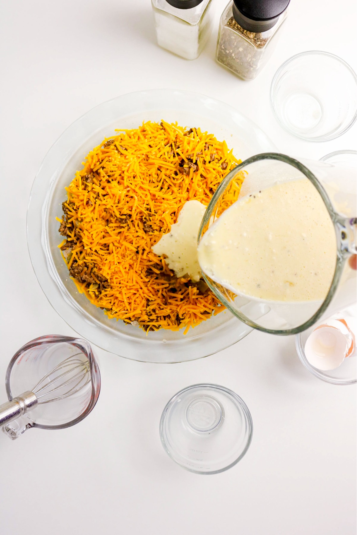 Pouring bisquick, milk and egg mixture over ground beef.