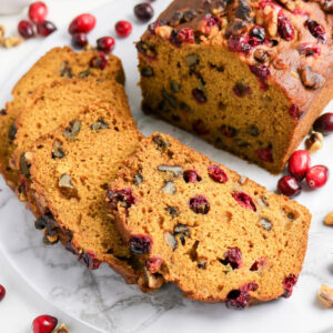 Sliced homemade pumpkin cranberry loaf on a marble serving platter.