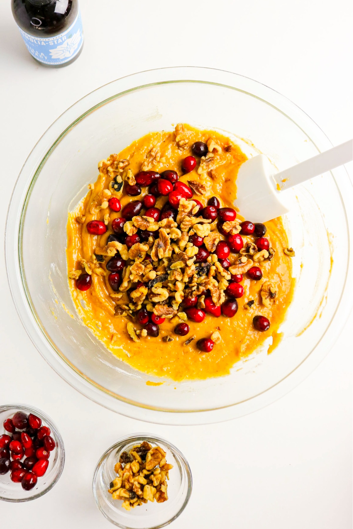 Pumpkin bread ingredients in a mixing bowl with chopped walnuts and fresh cranberries.