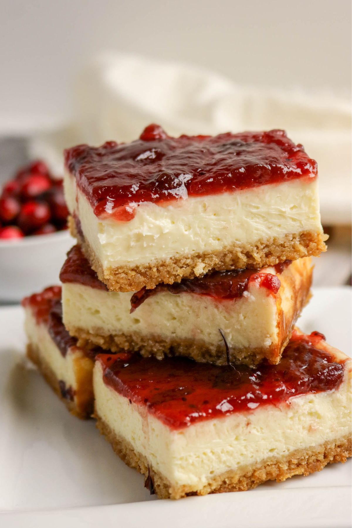 Three cheesecake bars with a graham cracker crust and a layer of cranberry sauce are stacked on a white plate.