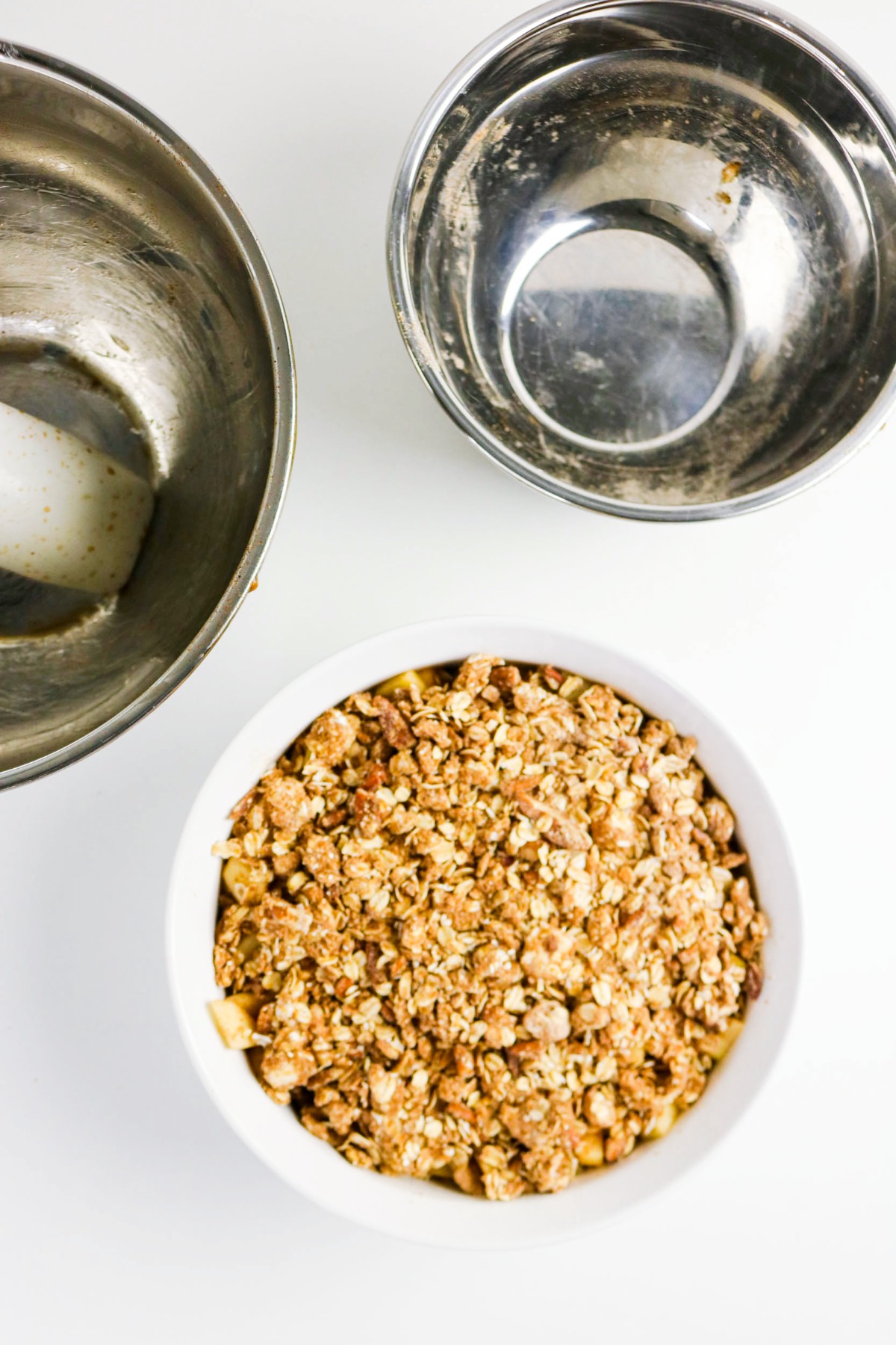 Apple crisp topping on apples in a white dish before baking.