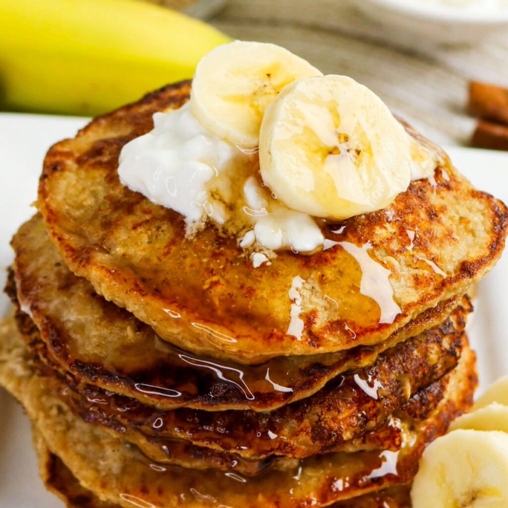 A stack of pancakes topped with banana slices a a dollop of cottage cheese.