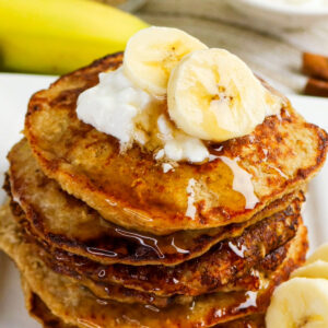 A stack of pancakes topped with banana slices a a dollop of cottage cheese.