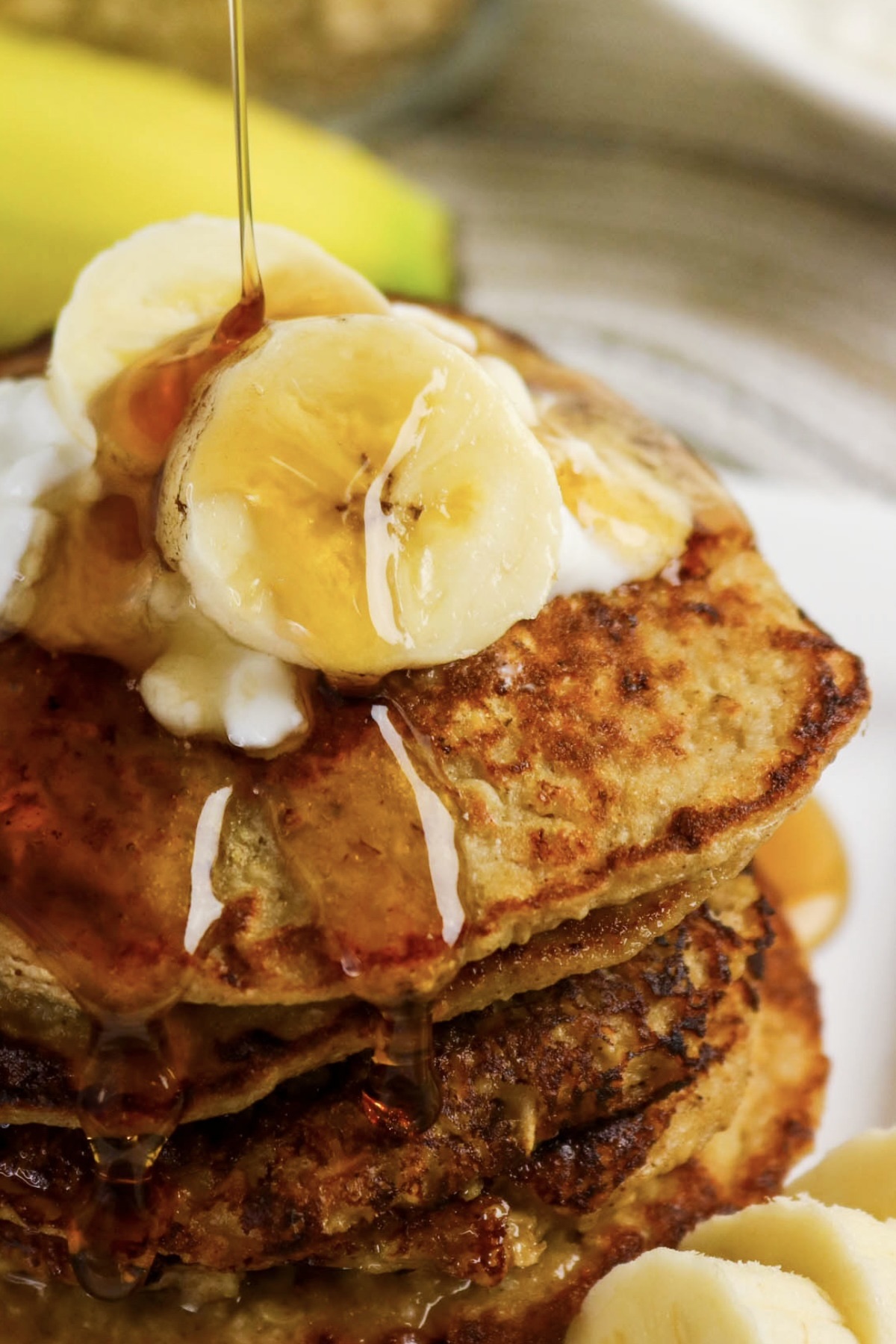 Close view of pancakes topped with sliced bananas and maple syrup.
