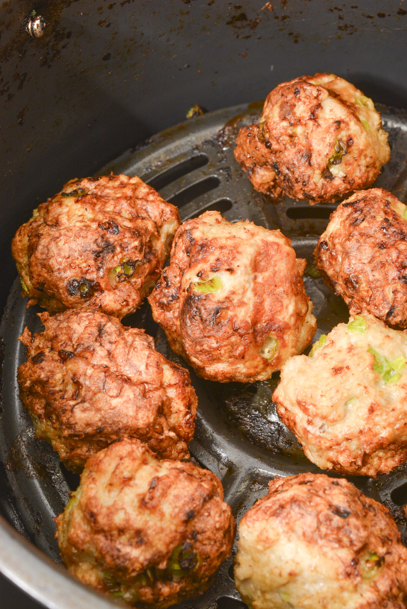 Cooked meatballs in an air fryer basket.