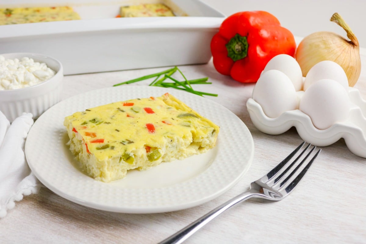 Slice of cooked baked egg casserole on a white plate with a fork on the side.