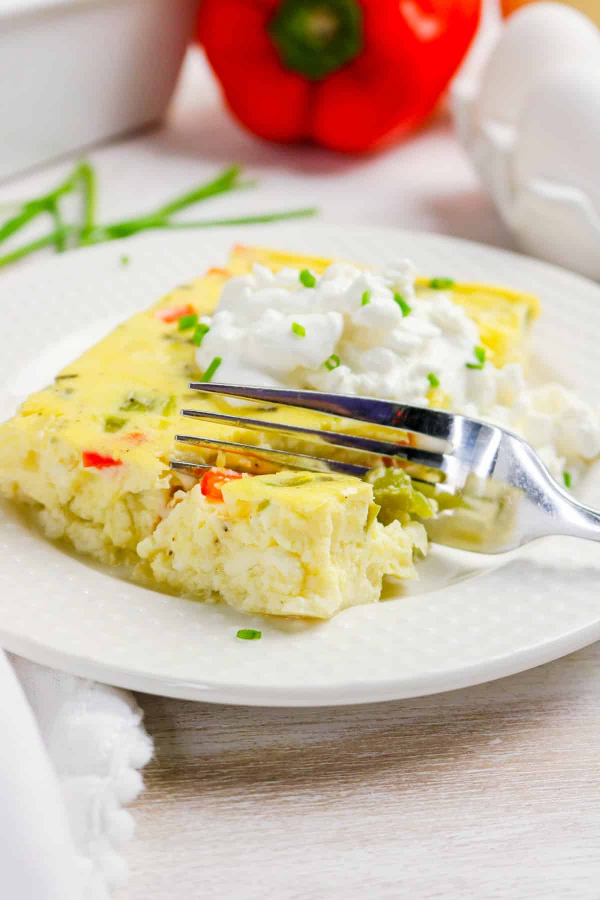 Slice of egg bake on a white plate topped with cottage cheese.