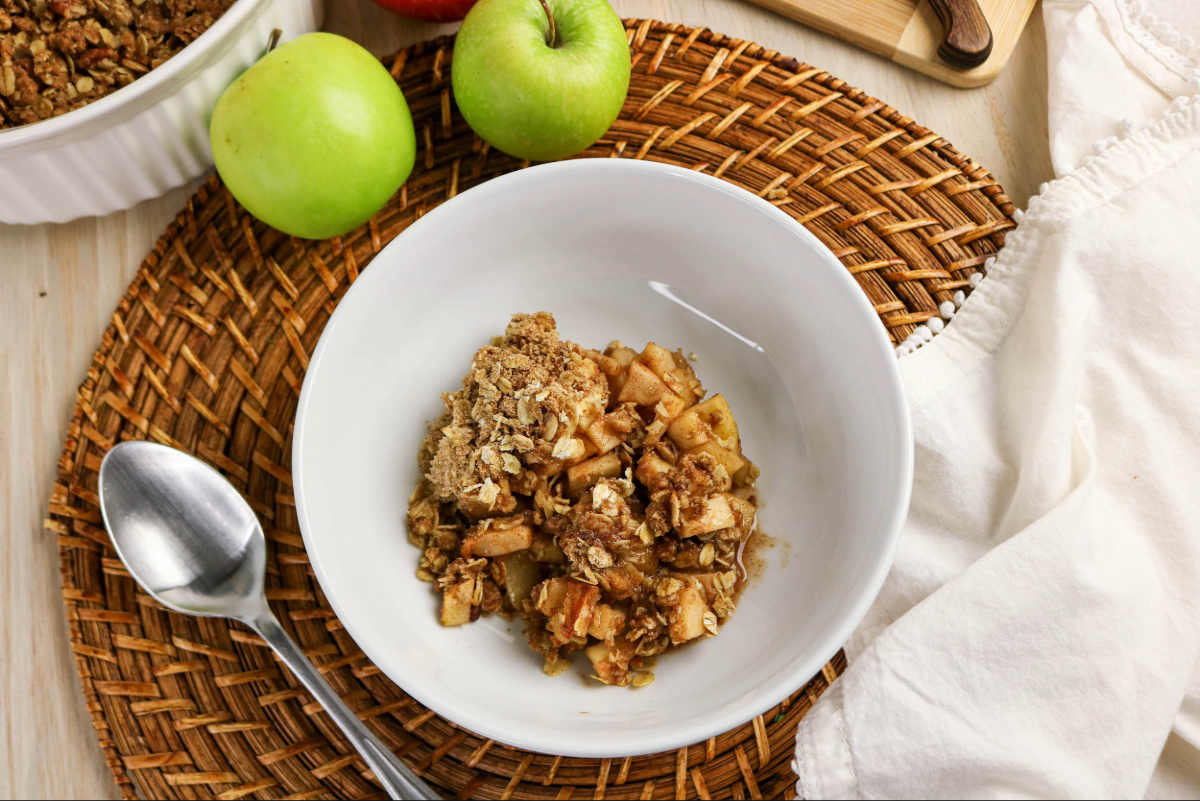 A serving of apple crisp with whole green apples on the side.