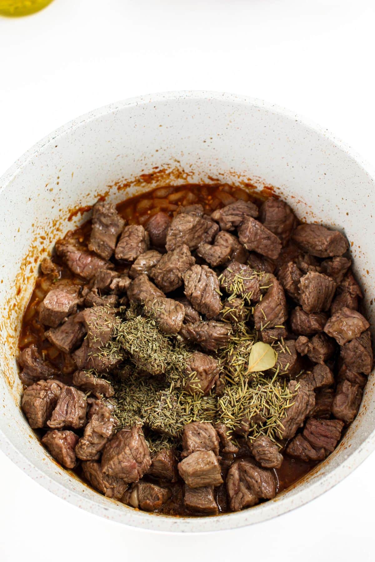 Browned beef brisket with dried herbs and bay leaf added to the pot.