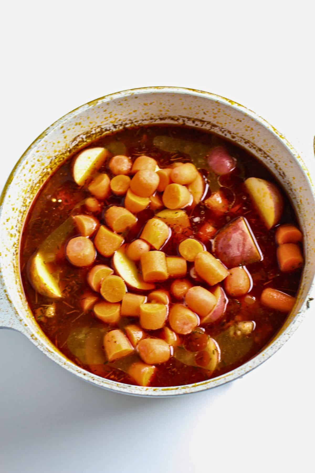 Carrots and potatoes added to broth simmering in Dutch oven.