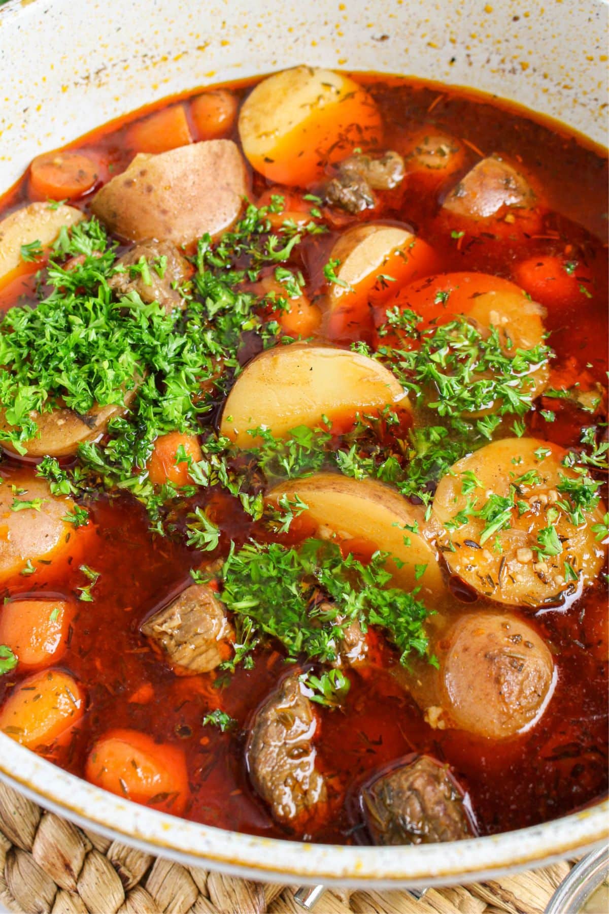 Beef brisket stew simmering in Dutch oven topped with fresh parsley.