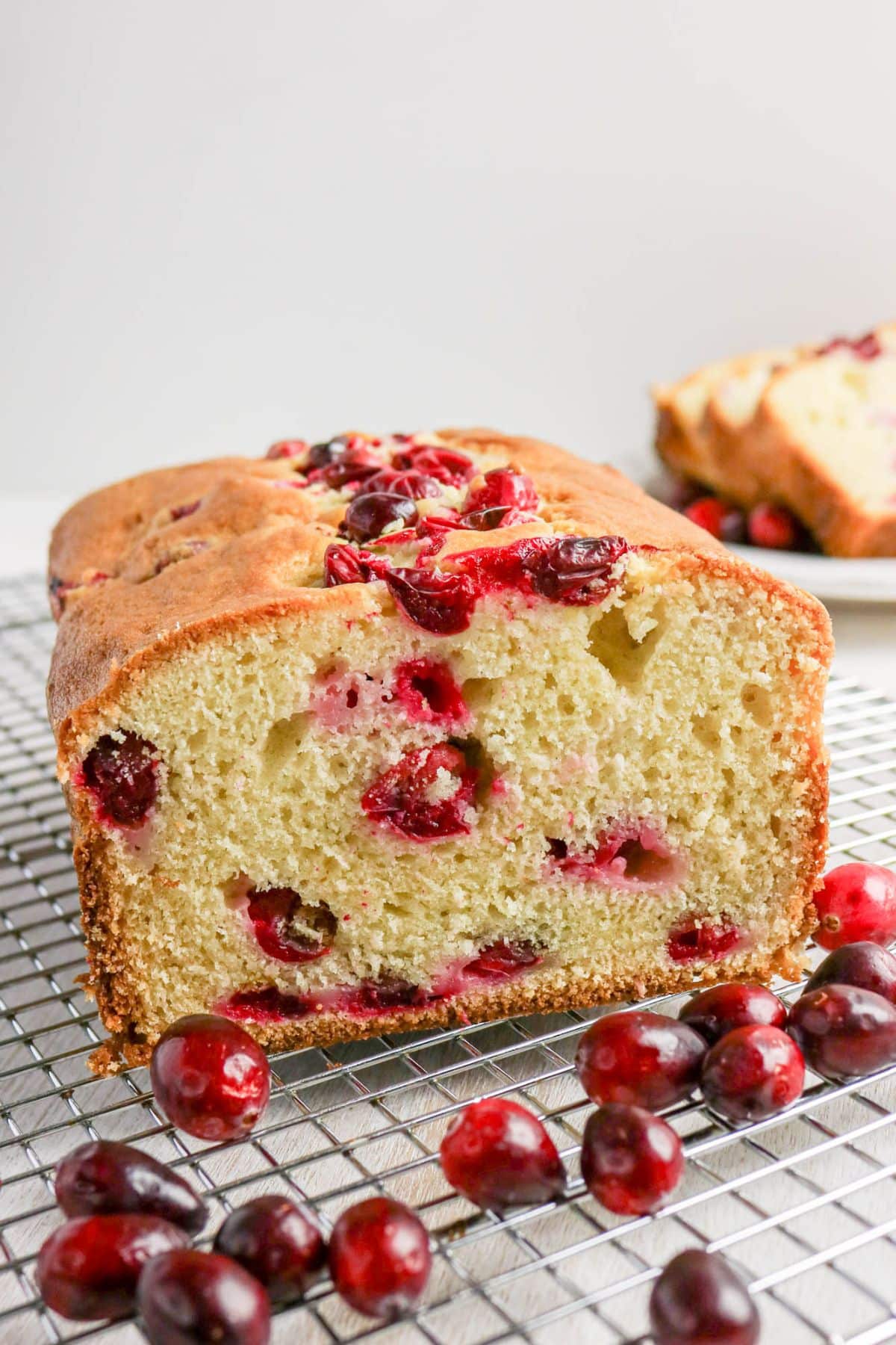 Loaf of cranberry cream cheese bread on a wire rack with a slice missing.
