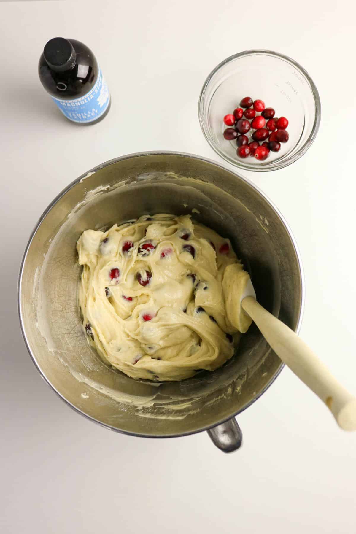 Cranberries being folded into batter in a metal mixing bowl.