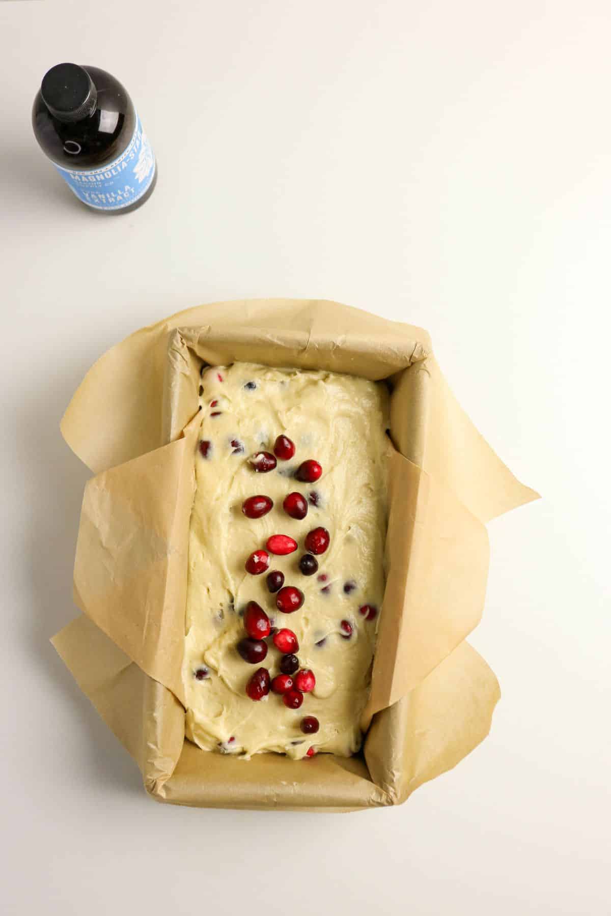 Batter with fruit sprinkled on top in a parchment lined loaf pan.