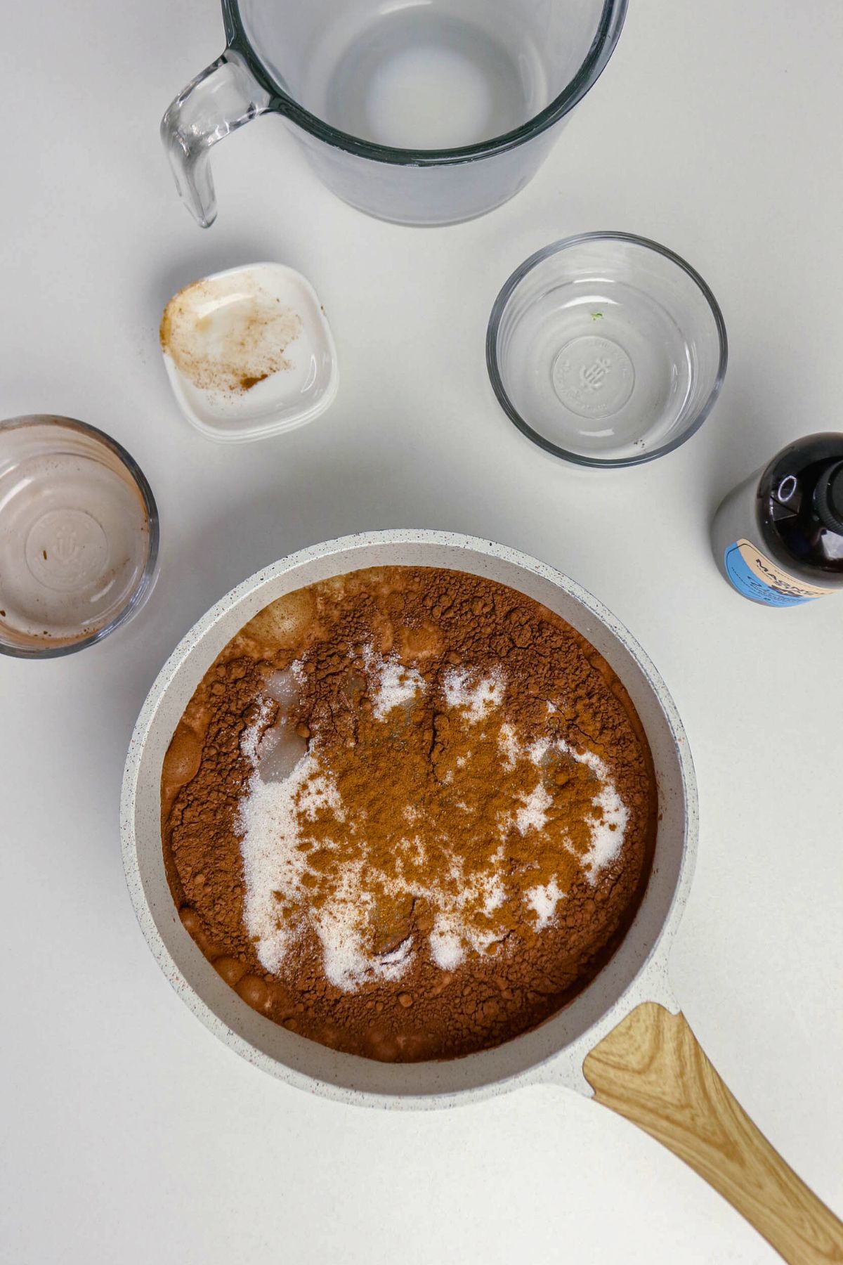 Cocoa powder, sugar, and spices added to hot chocolate in a saucepan.