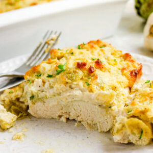 On a white dinner plate is baked chicken with artichoke hearts.