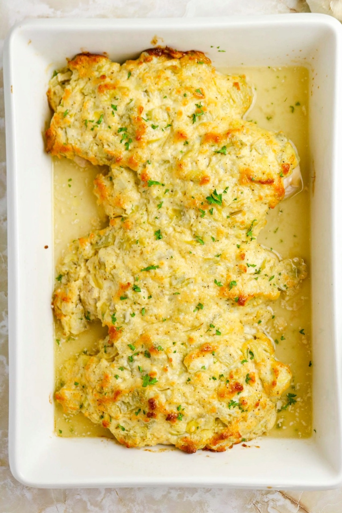 Artichoke chicken baked in a white casserole dish.