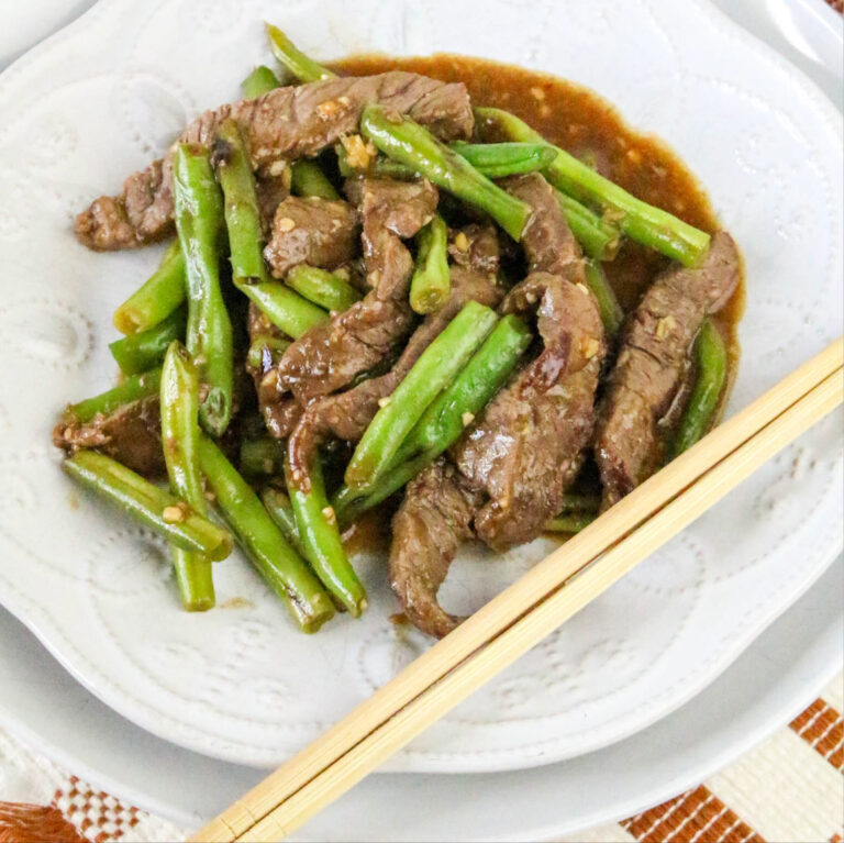 Cooked slices of beef with green beans on a white plate.