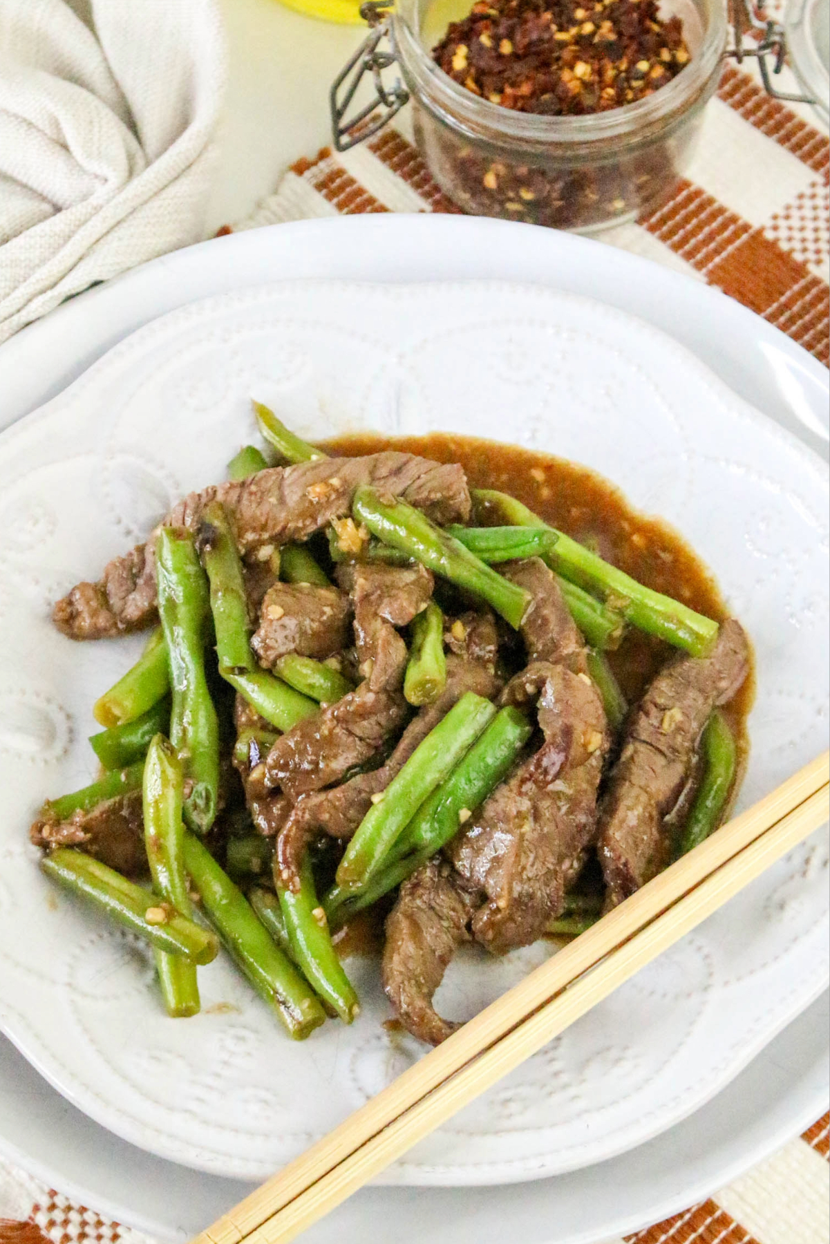 Beef and green beans in a white bowl with chopsticks on the side.