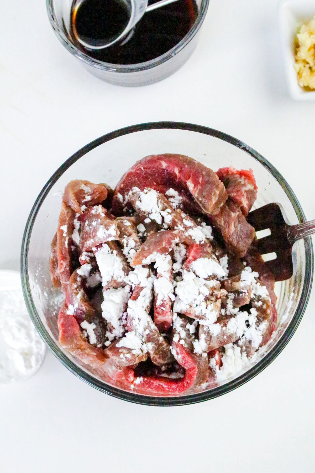 Sliced beef in a glass mixing bowl with cornstarch.